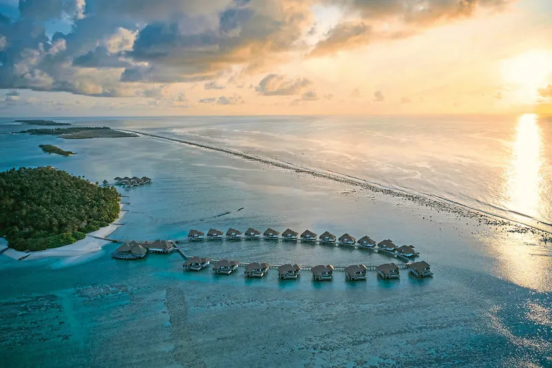 Zračni posnetek COMO Maalifushi z vodnimi vilami ob sončnem zahodu
